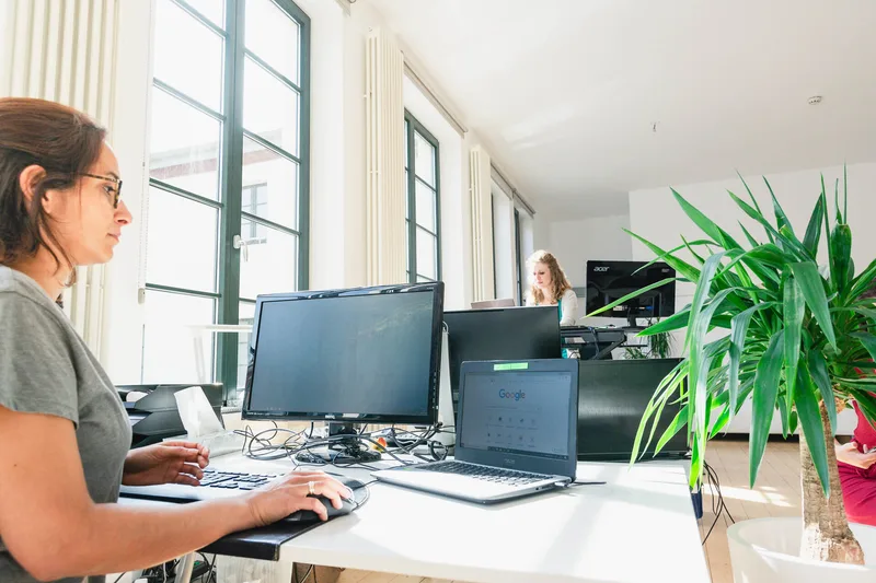 Zwei Personen arbeiten an Bildschirmen in einem hellen Büro.