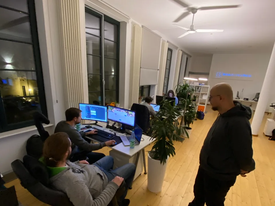 Abend im Mainzer Büro: mehrere Personen arbeiten an Bildschirmarbeitsplätzen entlang der Fensterfront.
